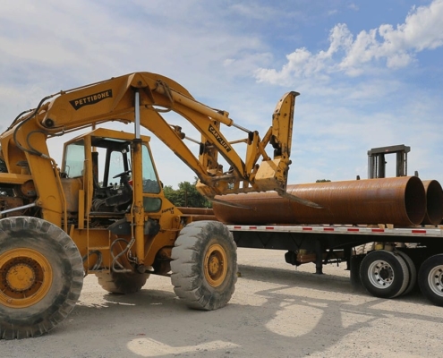 Front loader tractor loading large pipes on a truck